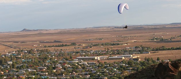 designer pool covers A person is soaring through the sky on a paraglider above a town.