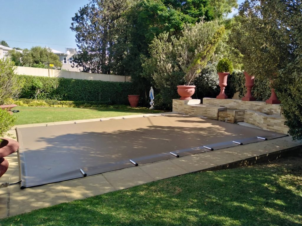 designer pool covers A backyard with a pool covered by pool covers.