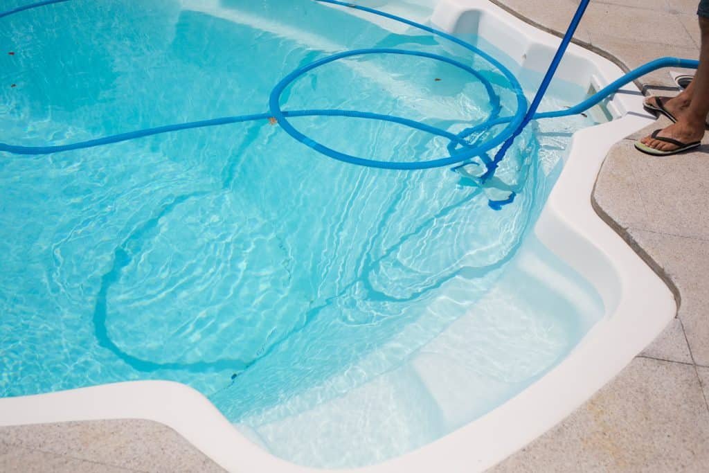 designer pool covers A person cleaning a swimming pool with a hose, utilizing pool covers to maintain cleanliness.