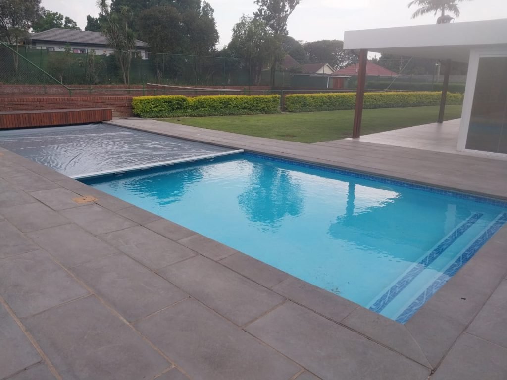 designer pool covers A backyard swimming pool featuring a deck and a pool cover reel.