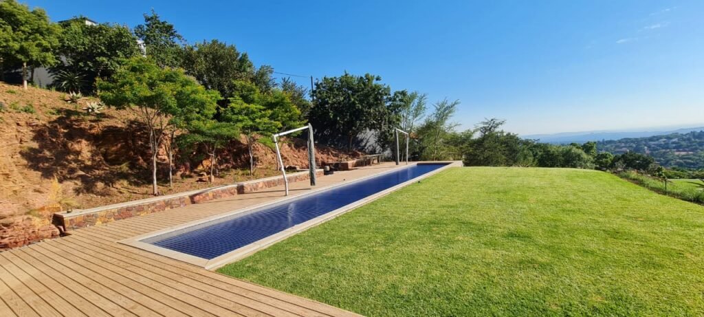 designer pool covers An infinity pool and wooden deck overlooking a scenic landscape with hills under a clear blue sky.